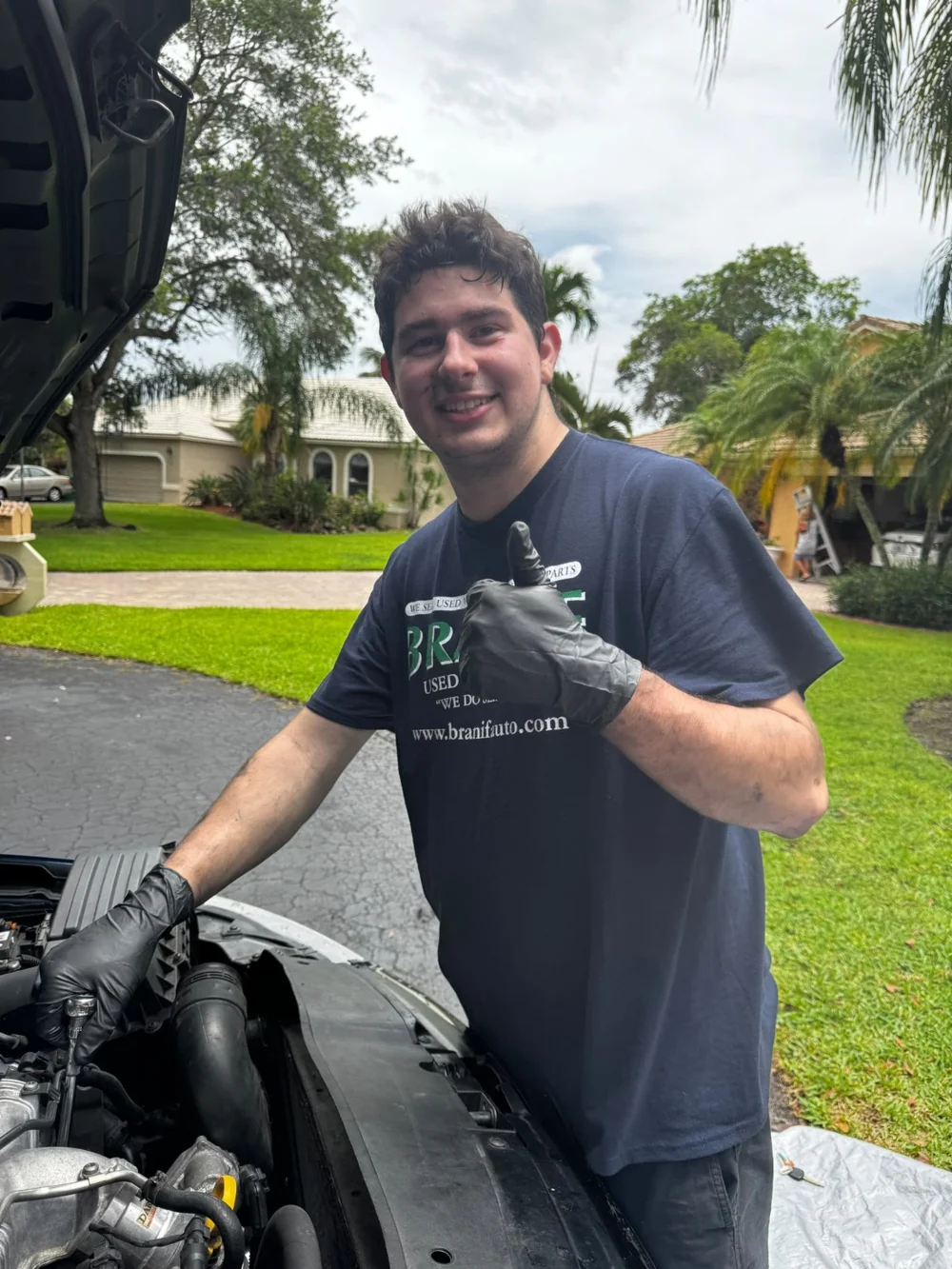 Josh beside an open engine bay in a driveway