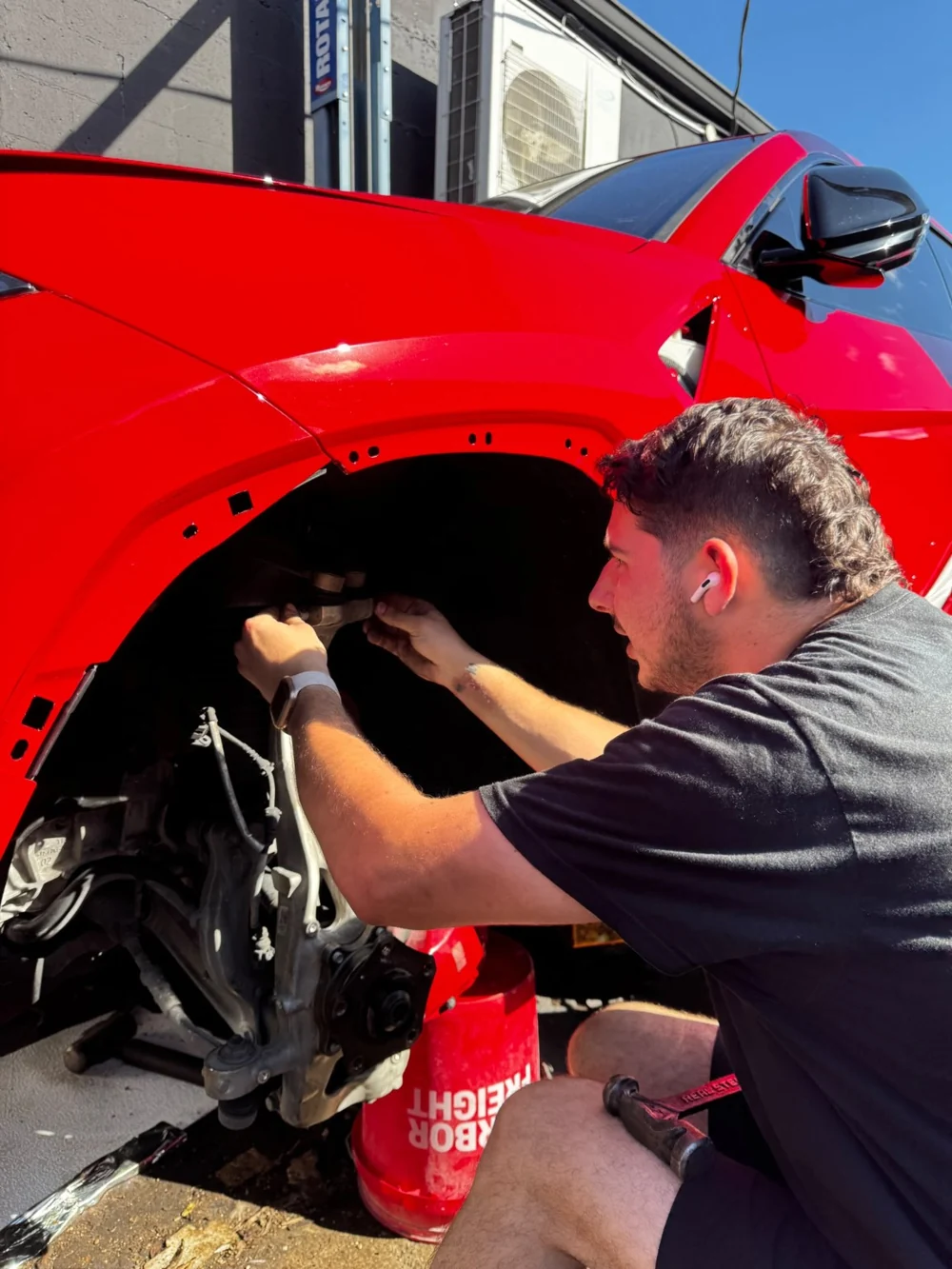 Josh working inside the front wheel well of a red vehicle